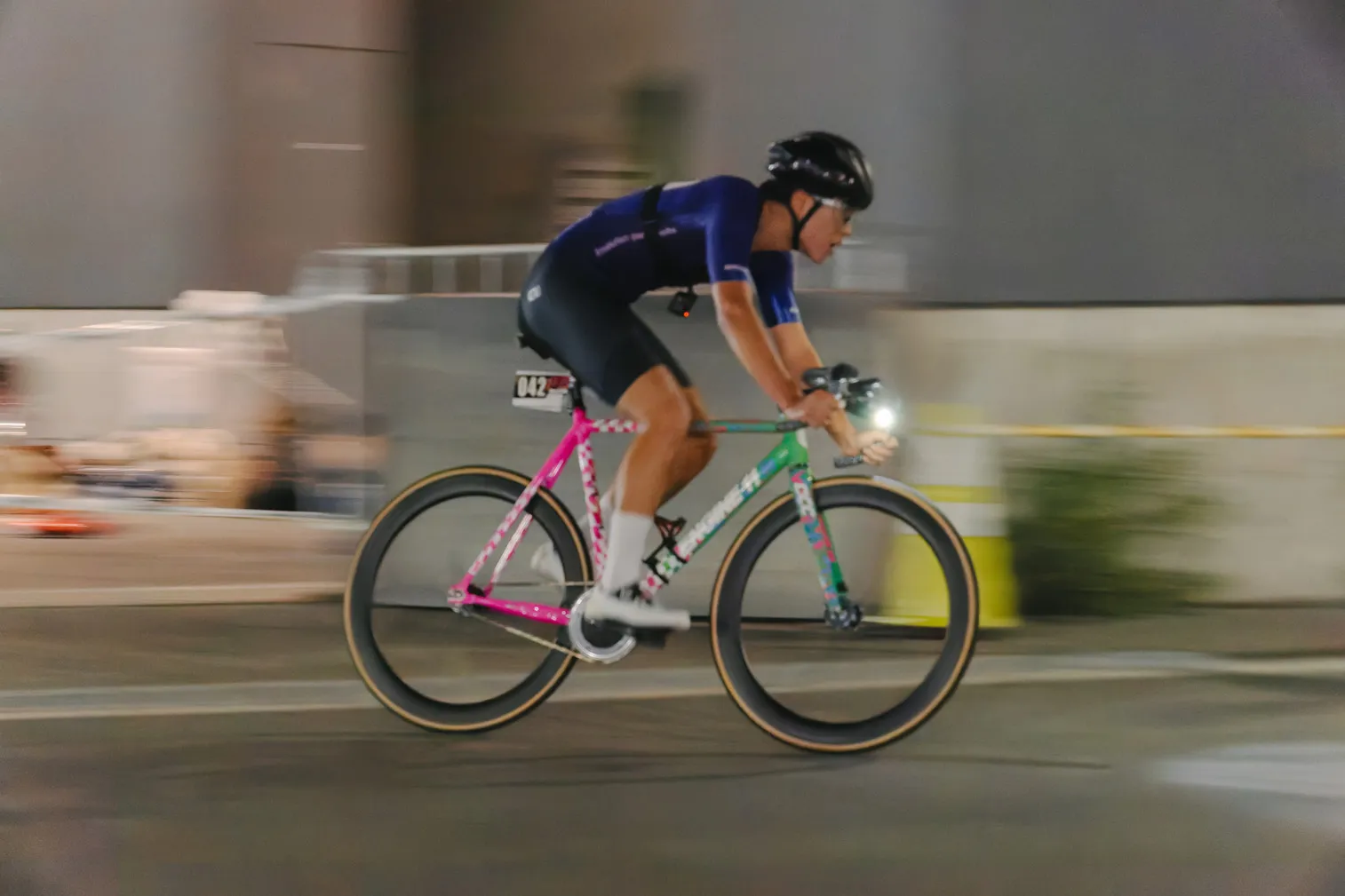 夜の街路で、青い服の自転車選手が走っている写真