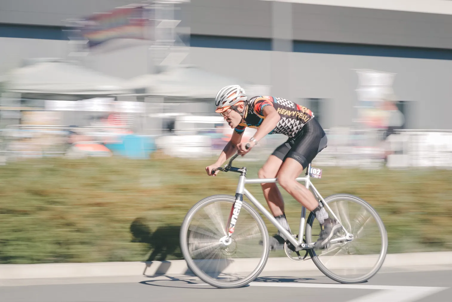 昼の道路で、白い服の自転車選手を流し撮りした写真