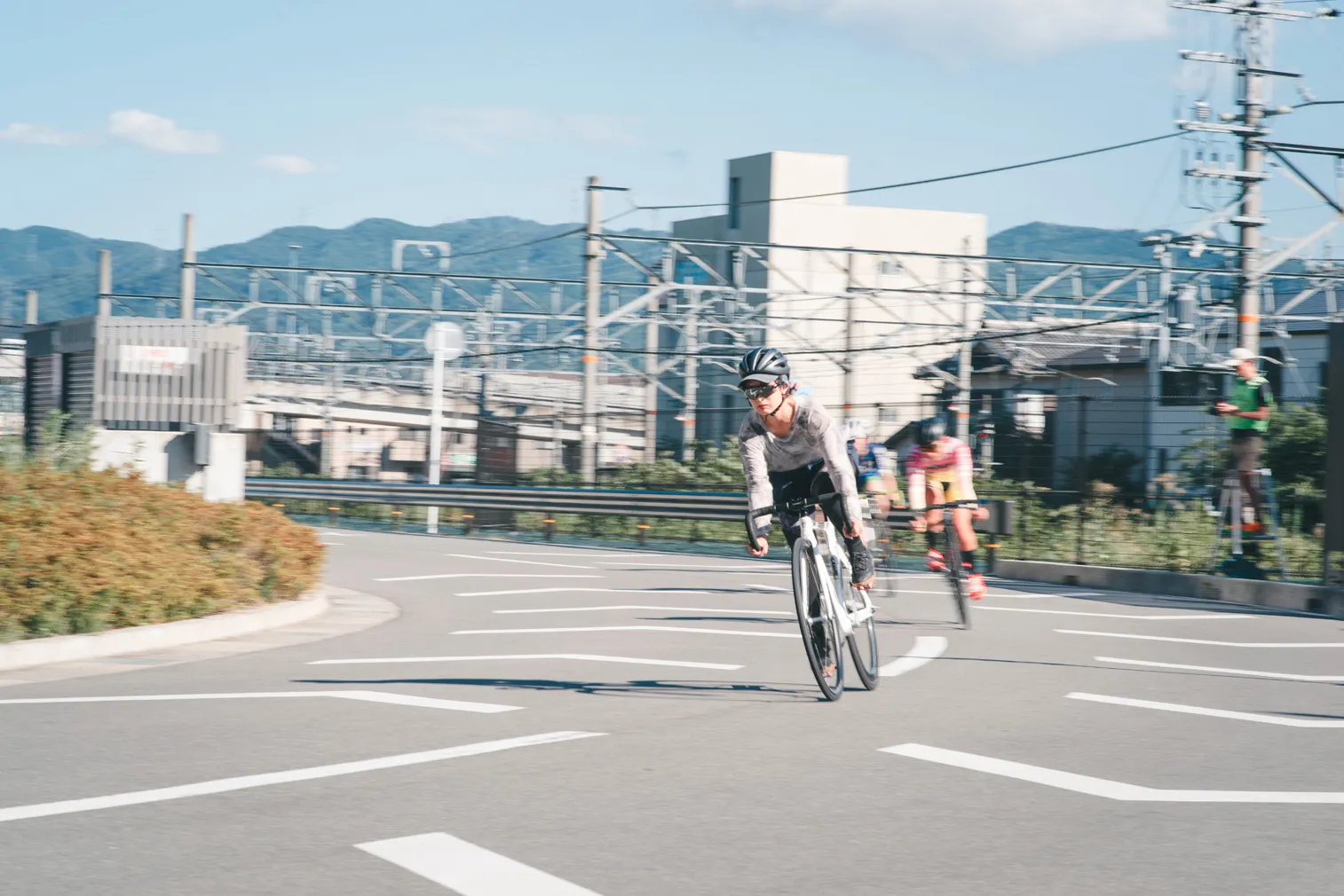 昼の交差点付近で、自転車選手と山並みを写した写真