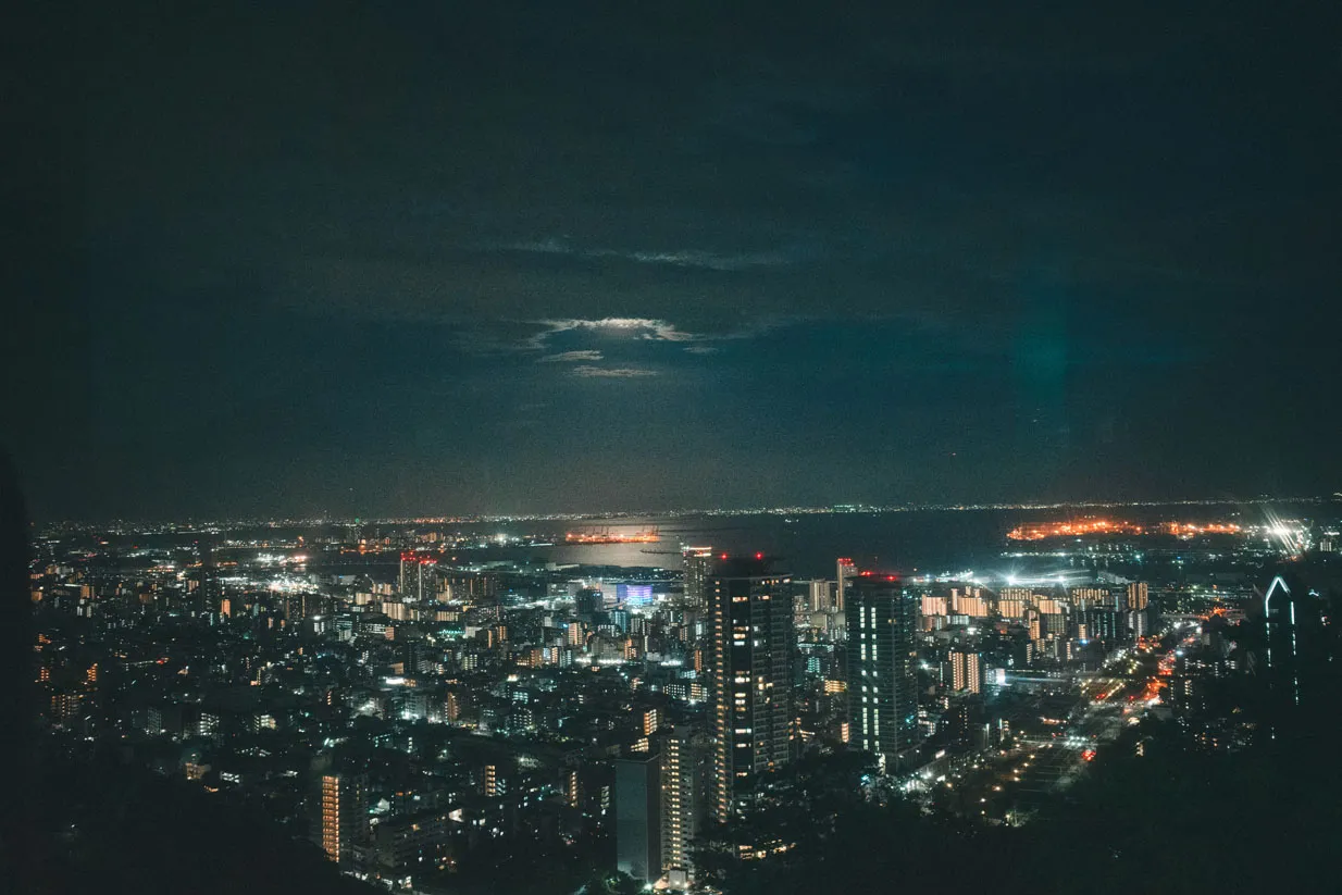 高い場所から、夜の街明かりと暗い山並みを写した写真