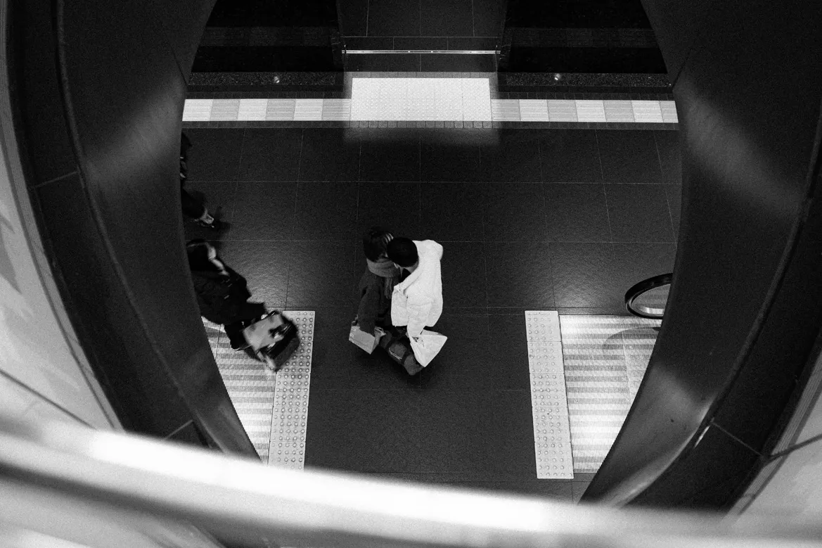 円形の開口部越しに、階段付近の人物を白黒で写した写真